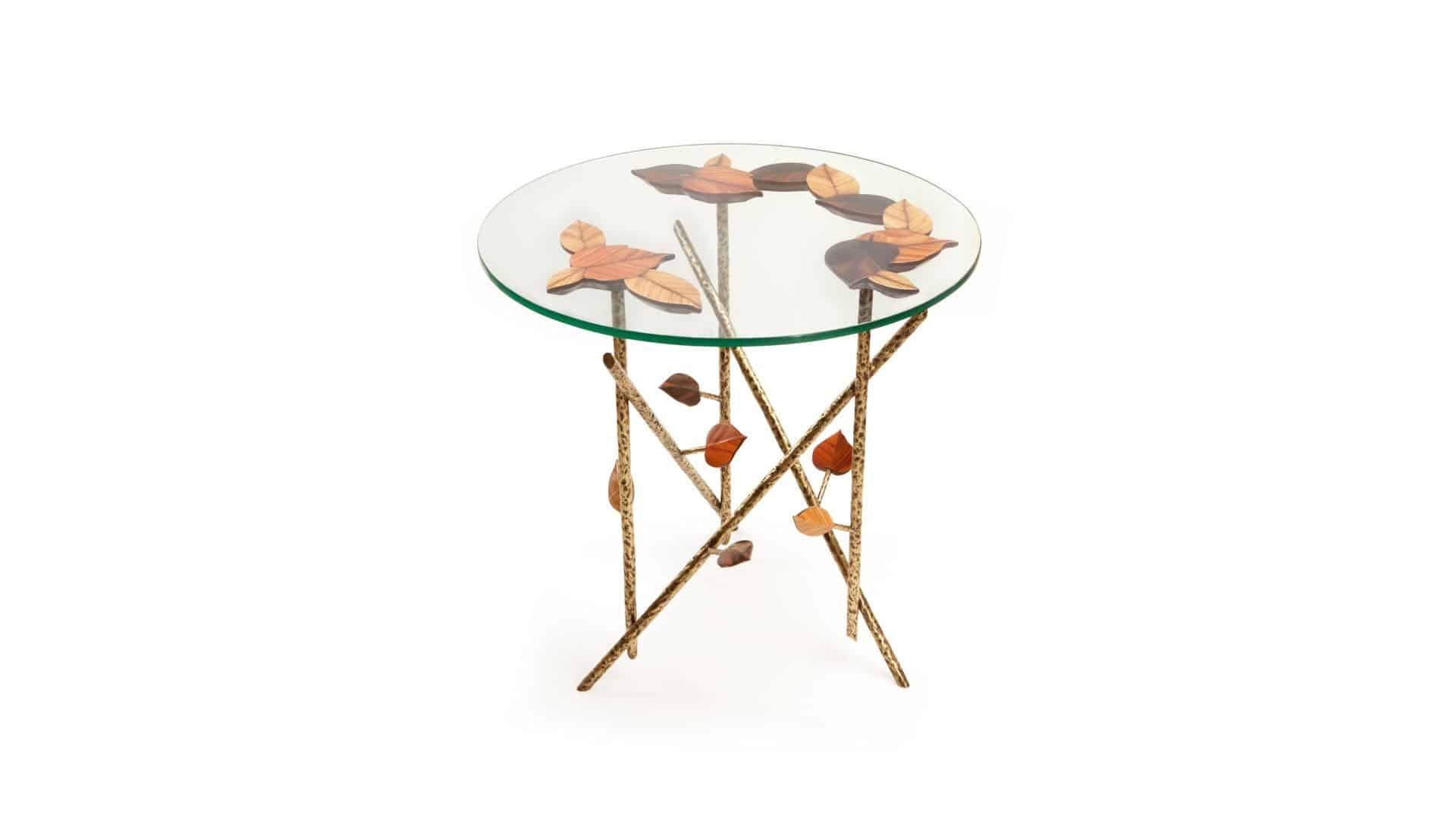 Mesa de cristal redonda con soportes dorados desiguales y dibujos de hojas.