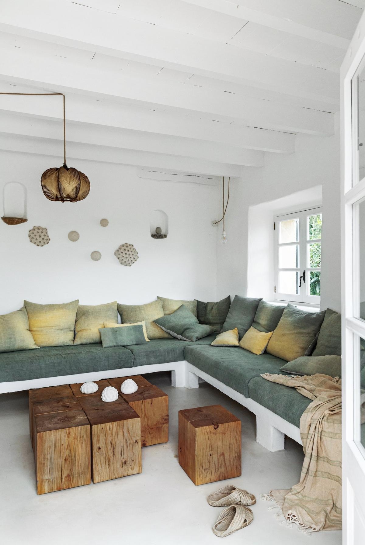 Salón en tonos blancos con sofá con cojines verdes y amarillos y cubos de madera formando una mesa.