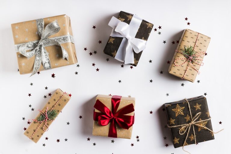 Seis cajas de regalo envueltos con papeles navideños de diferentes colores y estampados colocados sobre un fondo blanco con estrellas plateadas