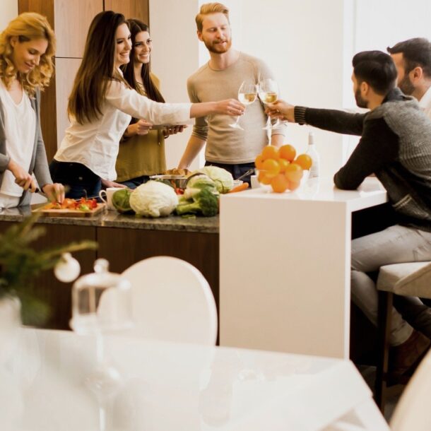 Grupo de personas brindando en una cocina moderna, rodeados de verduras frescas y frutas.