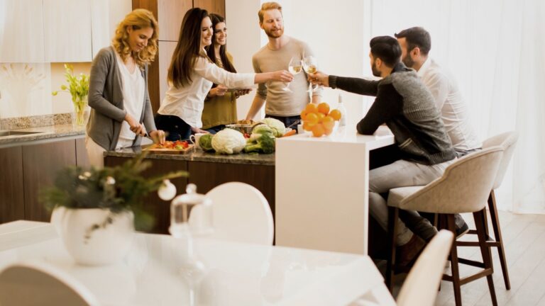 Grupo de personas brindando en una cocina moderna, rodeados de verduras frescas y frutas.