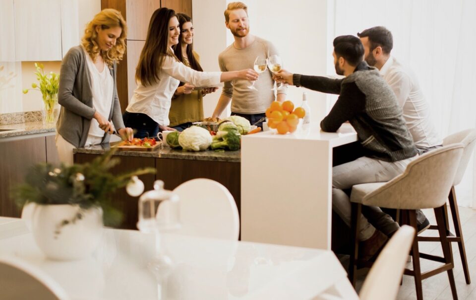 Grupo de personas brindando en una cocina moderna, rodeados de verduras frescas y frutas.